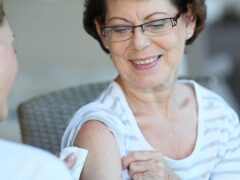 A medical professional prepares to give a vaccine to a an older woman patient.