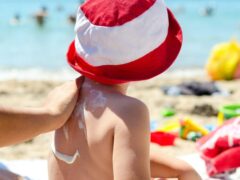 Young boy sitting on the beach having sunscreen applied to his back