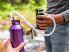 Man and woman couple using water filter on hiking trail river in Colorado to purify drinking water into bottle