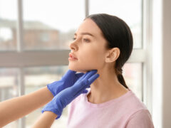Endocrinologist examining thyroid gland of young woman in clinic
