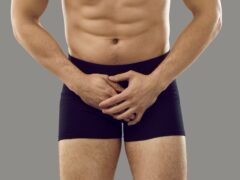 Man in underwear standing isolated on grey background covering his painful crotch area. Cropped shot, banner. Male intimate health problems, sexually transmitted diseases, testicular cancer concept