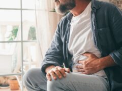 Man suffering with severe stomach pain sitting at home. Hand of mature guy holding abdomen suffering from ache, diarrhea or indigestive problem. Caucasian guy pressing on belly on painful sensation