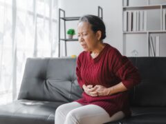 Elderly asian housewife woman sitting on sofa. Abdominal pain, gastritis, appendicitis