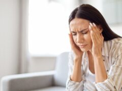 Headache Concept. Young stressed woman suffering from migraine at home, sick millennial female rubbing temples while sitting on couch in living room, feeling unwell, having acute pain, closeup shot