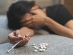 Anti drug, drug addict asian young woman, girl hand holding for syringe, medicament with narcotic on couch at home, abuse overdose. Sick pain of health, unhealthy people. Suicide depressed or despair