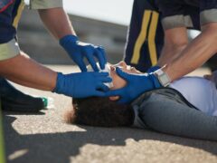 Paramedic, accident and hands on head injury on road in car crash emergency with healthcare people. EMS, wrapping bandage or first responder with victim or rescue in street for transport to hospital