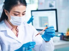 Female scientist in protective mask and gloves analyzing blood samples in test tubes inside a modern laboratory, symbolizing medical diagnostics, healthcare research, and scientific innovation.