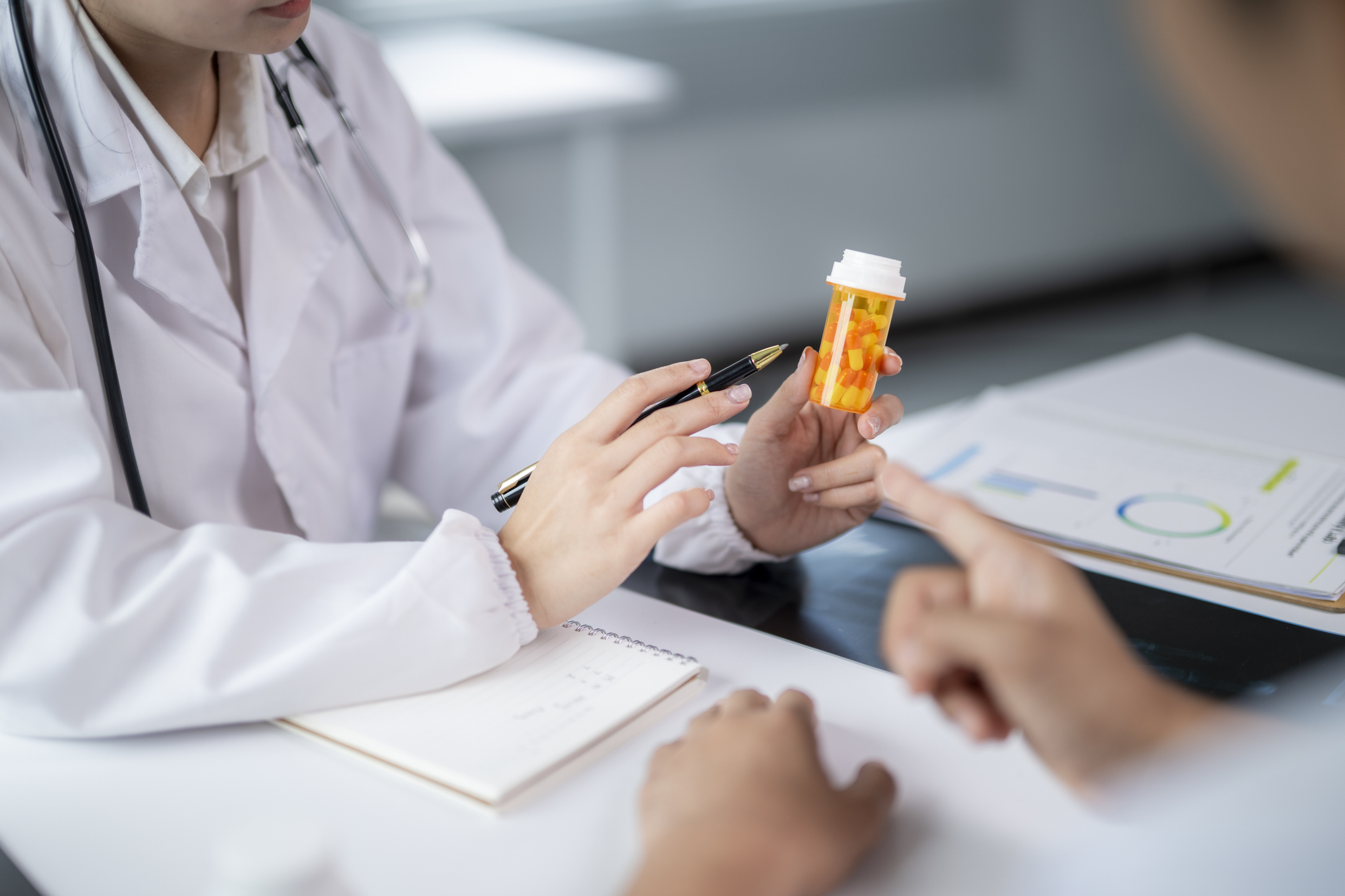 Doctor holding medicine bottle and pen, explaining prescription to patient